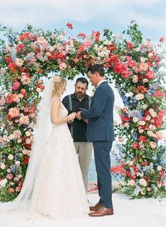 a bride and groom standing in front of a floral arch