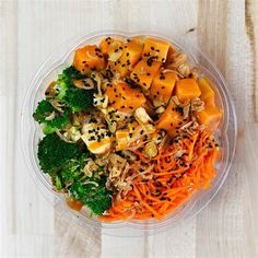 a plastic bowl filled with carrots, broccoli and other vegetables on top of a wooden table