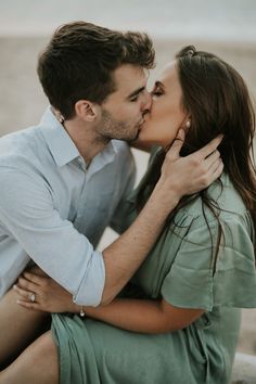 a man kissing a woman on the cheek while sitting in front of an ocean shore