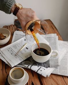 a person pouring coffee into a cup on top of newspapers