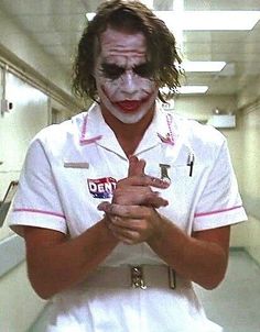 a man dressed as the joker is standing in a hallway with his hands clasped together