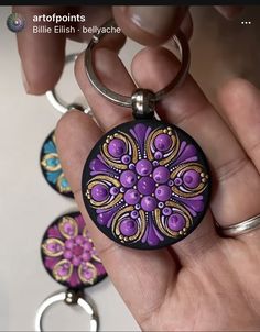 a hand holding a purple and black keychain with three different designs on it