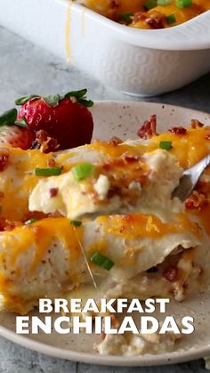 a white plate topped with enchiladas covered in cheese and sauce next to a bowl of strawberries