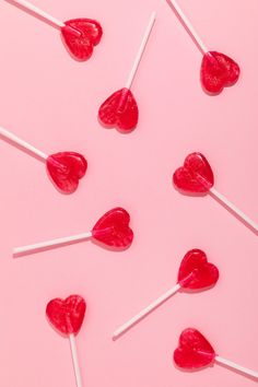 lollipops in the shape of hearts are on a pink surface with white sticks