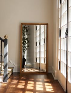 a large mirror sitting on top of a wooden floor next to a stair case and window