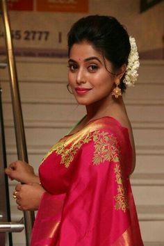 a woman in a red and gold sari posing for the camera while holding a pole