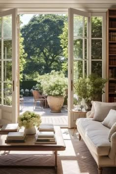 a living room filled with lots of furniture next to a large open window covered in plants