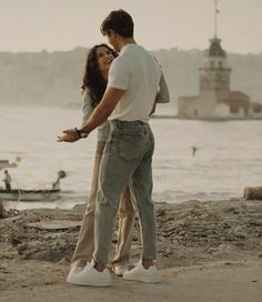 a man and woman standing next to each other near the water