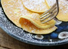 a plate with pancakes and powdered sugar on it, being held by a fork