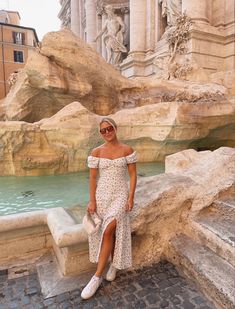 a woman in a white dress standing on steps next to a fountain with statues behind her