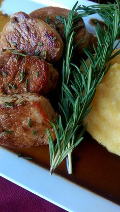 some meat and potatoes on a plate with green sprig garnishes