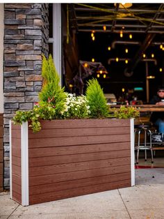 a large wooden planter filled with flowers and greenery next to a restaurant entrance