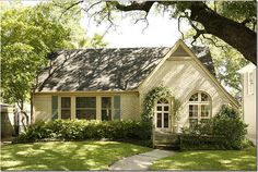 a small house with green shutters and trees in the front yard on a sunny day