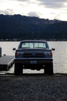 a pickup truck parked next to a body of water with a dock in the background