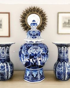 three blue and white vases sitting on top of a wooden table next to framed pictures