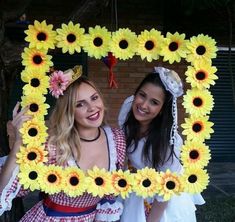 two women dressed in costumes holding up a frame with sunflowers on it