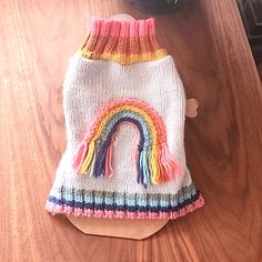 a knitted dog sweater with a rainbow design on the front and side, sitting on a wooden table