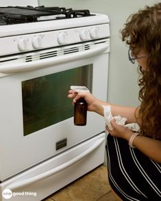 a woman is cleaning an oven with a rag and bottle in her hand as she opens the door