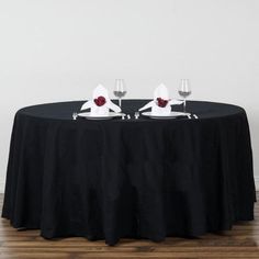 two wine glasses sitting on top of a black table with white napkins and red roses