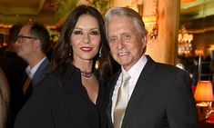 an older man and young woman posing for a photo in front of other people at a formal event