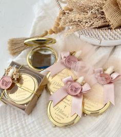 three wedding favors are sitting on a white tablecloth next to some gold and pink decorations