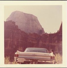 an old photo of a car parked in front of a large rock formation with a dog sitting on the hood