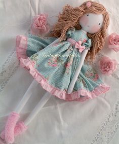 a doll laying on top of a white bed next to pink flowers and laces