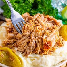 a plate with mashed potatoes topped with shredded pork and garnished with pickles