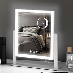 a lighted mirror with the image of a bed and pillows on it next to a bottle of perfume