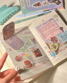 a hand holding an open notebook with stickers on it and various other items in the background