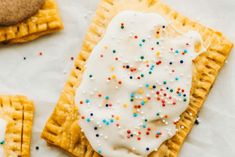 two waffles with white frosting and sprinkles on them next to cookies