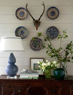 a table topped with blue vases and plates next to a wall mounted deer head