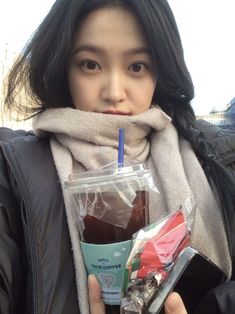 a young woman holding a cup of coffee and a drink in her hand while wearing a scarf