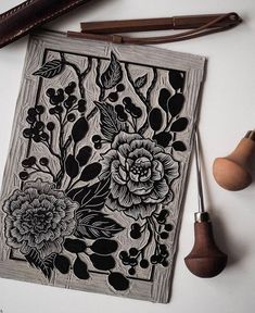 an intricately designed wood block with flowers and leaves on it, next to some leather crafting tools