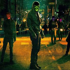 a group of masked people standing in the middle of a street at night with neon lights