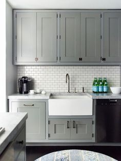 a kitchen with gray cabinets and white tile backsplash, stainless steel sink and dishwasher