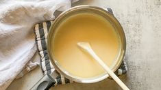 a pot filled with liquid next to a wooden spoon on top of a towel and cloth