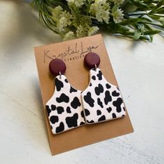 a pair of black and white animal print earrings on top of a card next to flowers