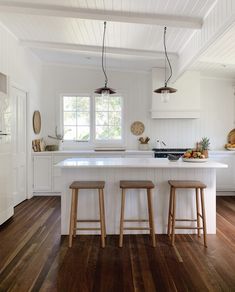 two stools sit at the center of a kitchen island with white cabinets and wood flooring