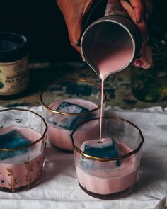 a person pouring pink liquid into small glasses