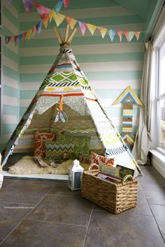 a teepee tent sitting on top of a floor next to a basket filled with books