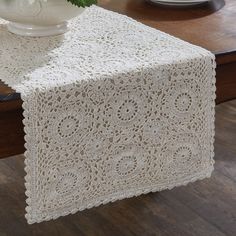 a white vase sitting on top of a table next to a lace covered table runner