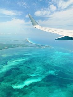 an airplane wing flying over the ocean with blue water and corals in the foreground