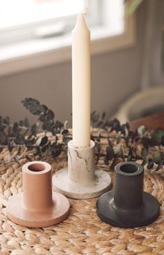 a white candle sitting on top of a table next to two black candlesticks