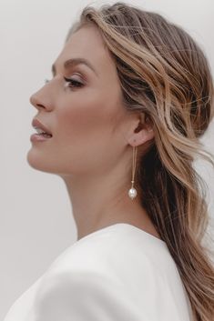 a woman with long hair wearing earrings and a white top is looking off to the side