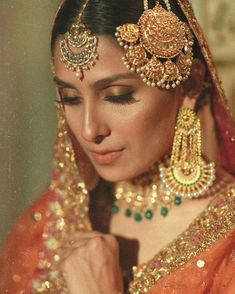 a woman in an orange bridal outfit with jewelry on her head and hands near her face