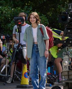 a woman standing in front of a camera on the street with other people behind her