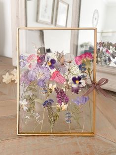 a glass frame with flowers in it sitting on a wooden floor next to a mirror