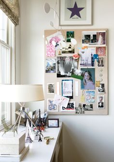 a white desk topped with a lamp next to a wall covered in pictures and photos