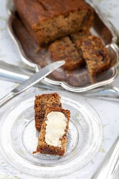 two slices of banana bread on a glass plate with butter and spoons next to it